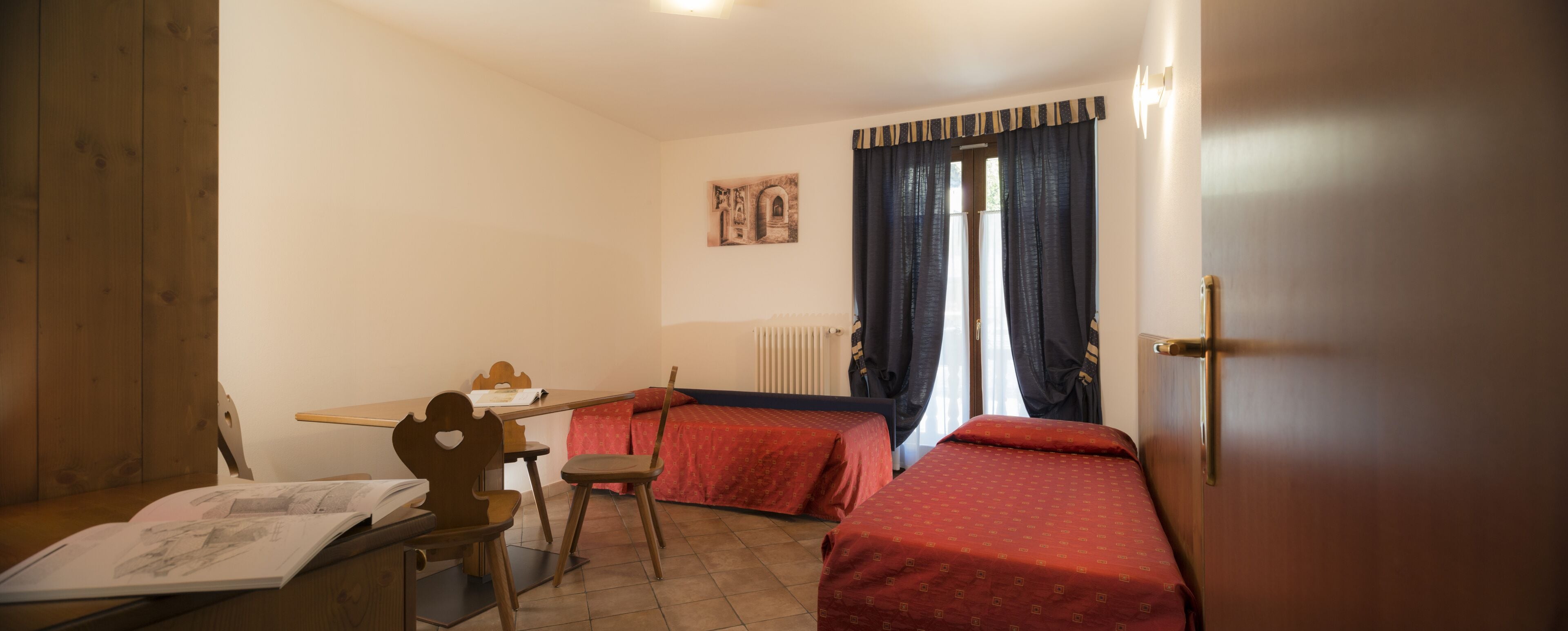 A room with two beds, a wooden desk, a chair, and a radiator.