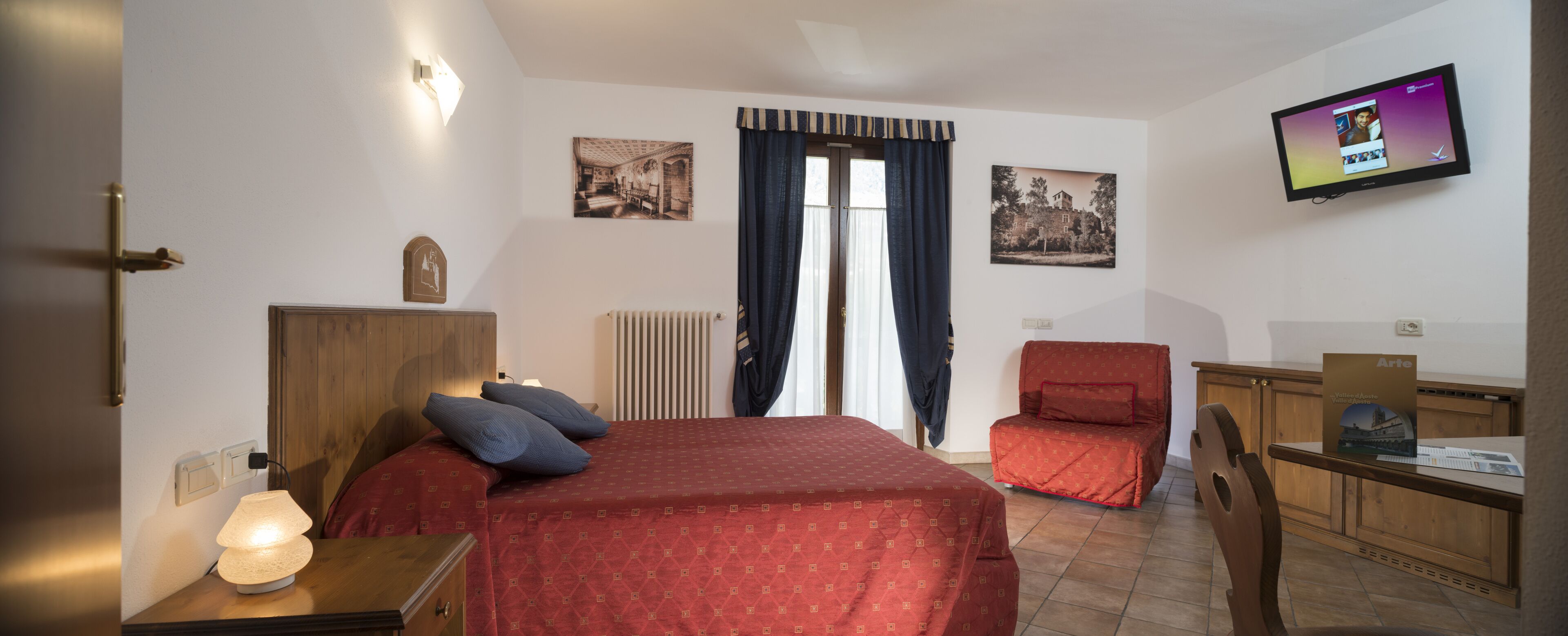 A hotel room with a bed, a desk, a chair, a television, and two framed pictures on the wall.