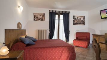 A hotel room with a bed, a desk, a chair, a television, and two framed pictures on the wall.