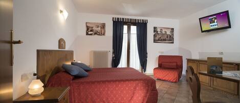 A hotel room with a bed, a desk, a chair, a television, and two framed pictures on the wall.