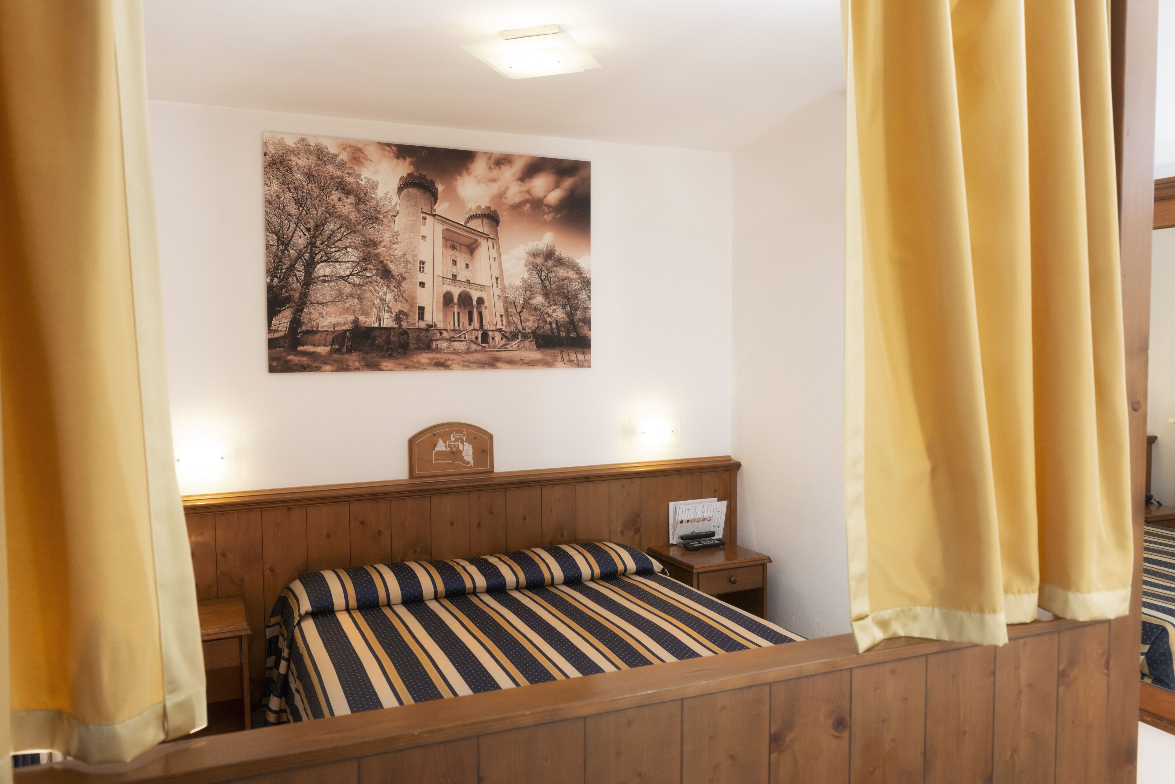 Una camera da letto con una testiera in legno, un letto con lenzuola a righe, un comodino con una lampada e un quadro appeso al muro raffigurante un castello.