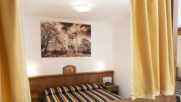 Una camera da letto con una testiera in legno, un letto con lenzuola a righe, un comodino con una lampada e un quadro appeso al muro raffigurante un castello.