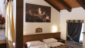 A bedroom with a wooden headboard, a bed with white linens, a nightstand, a lamp, a window with curtains, and a wall-mounted picture of a castle. - Chateau (Saint-Pierre)