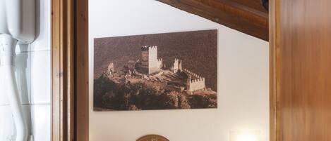 Een kamer met een bed, een houten plafond, een aan de muur hangend schilderij en een nachtkastje met een boek.