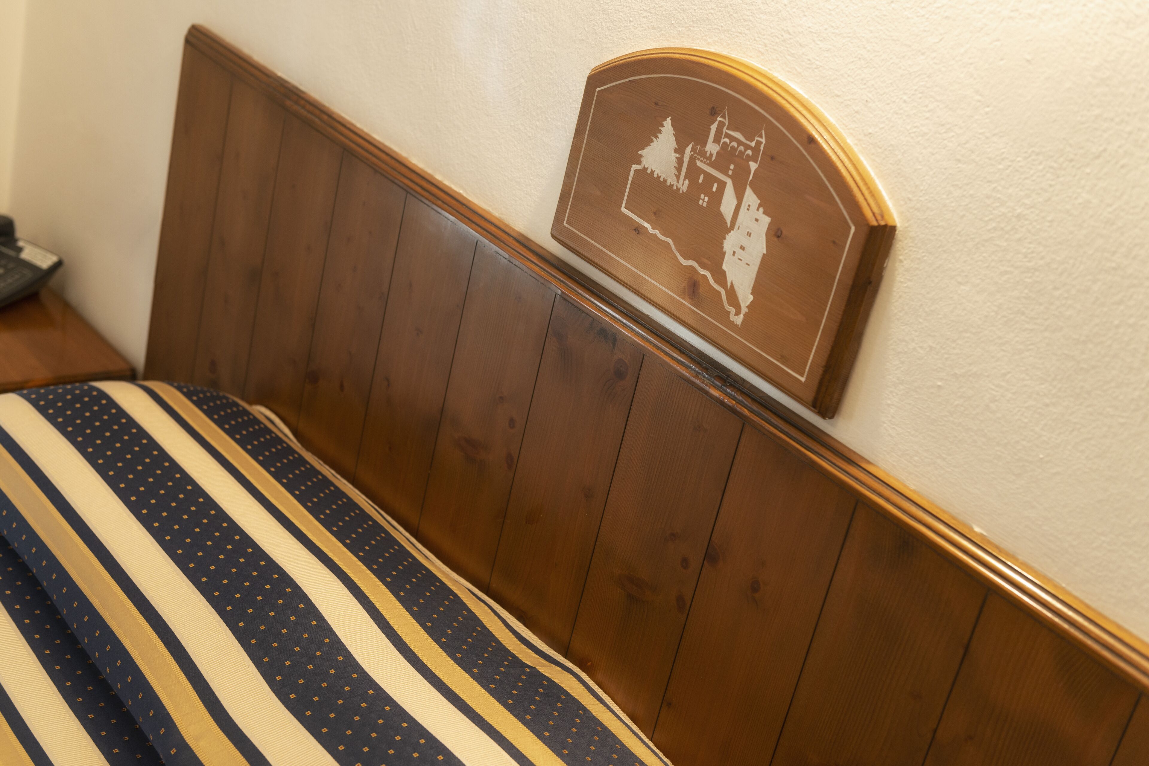 A wooden headboard with a castle design, a striped bedspread, and a wooden nightstand with a telephone.