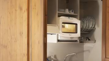 Una puerta de madera que da a una cocina con microondas, lavaplatos y estantes.
