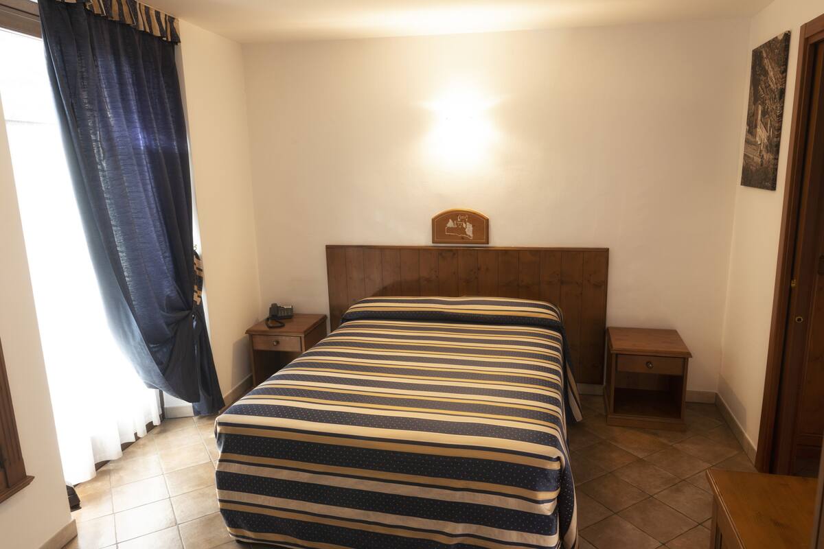 A bedroom with a bed, a nightstand, a wooden headboard, a wall clock, and a door.