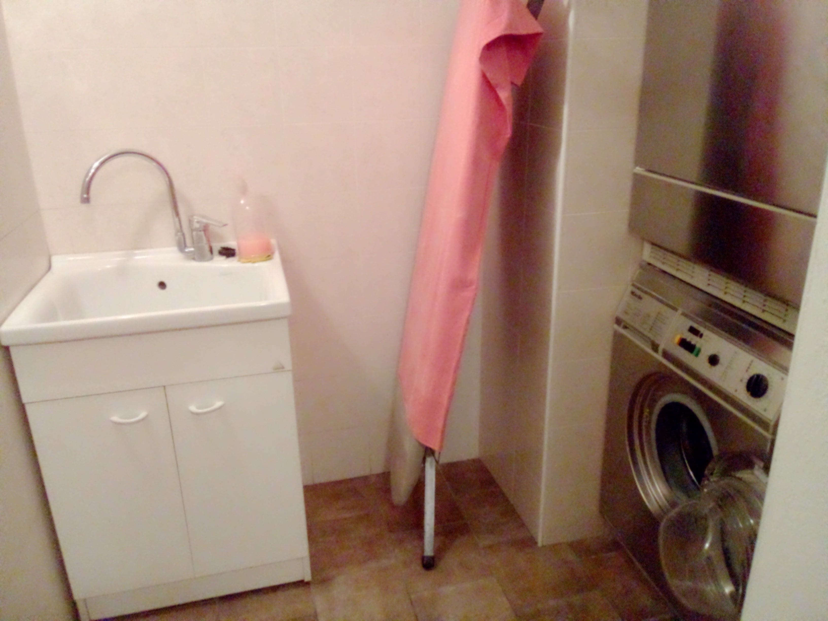 Un baño pequeño con lavamanos, lavadora y una toalla rosa colgada en la pared.