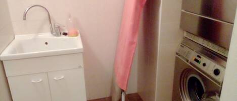 A compact bathroom with a sink, a washing machine, and a pink towel hanging on the wall.