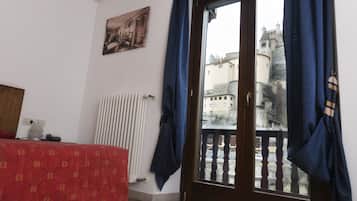Un dormitorio con cama, radiador, ventana con cortinas y vistas a un castillo a través de la ventana.