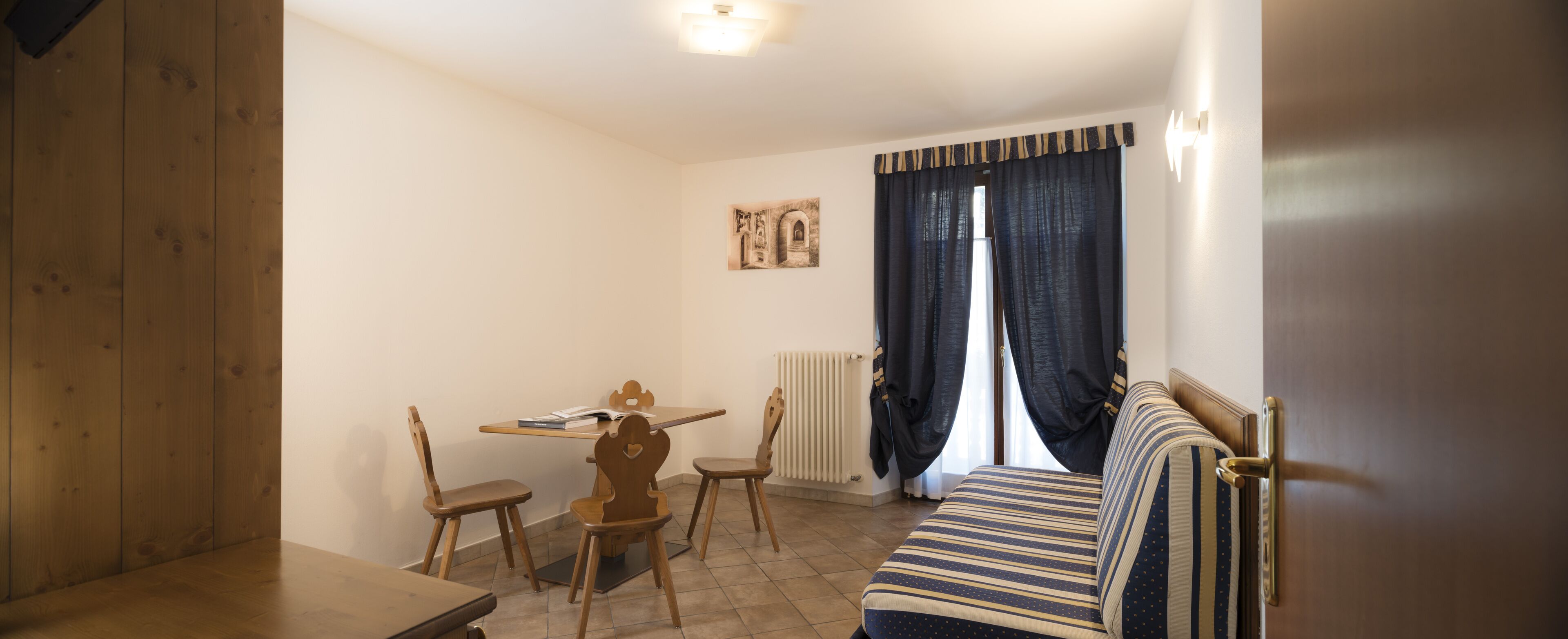 A small, cozy room with a wooden table, two chairs, a striped sofa, and a radiator.