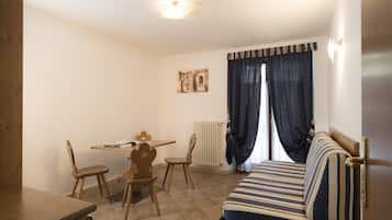 A small, cozy room with a wooden table, two chairs, a striped sofa, and a radiator.