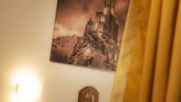A framed picture of a castle on a mountain, a wall-mounted light, and a small emblem below the picture.