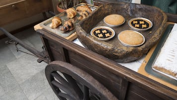 A rustic wooden cart with a tray holding croissants and three small metal pans with baked goods.