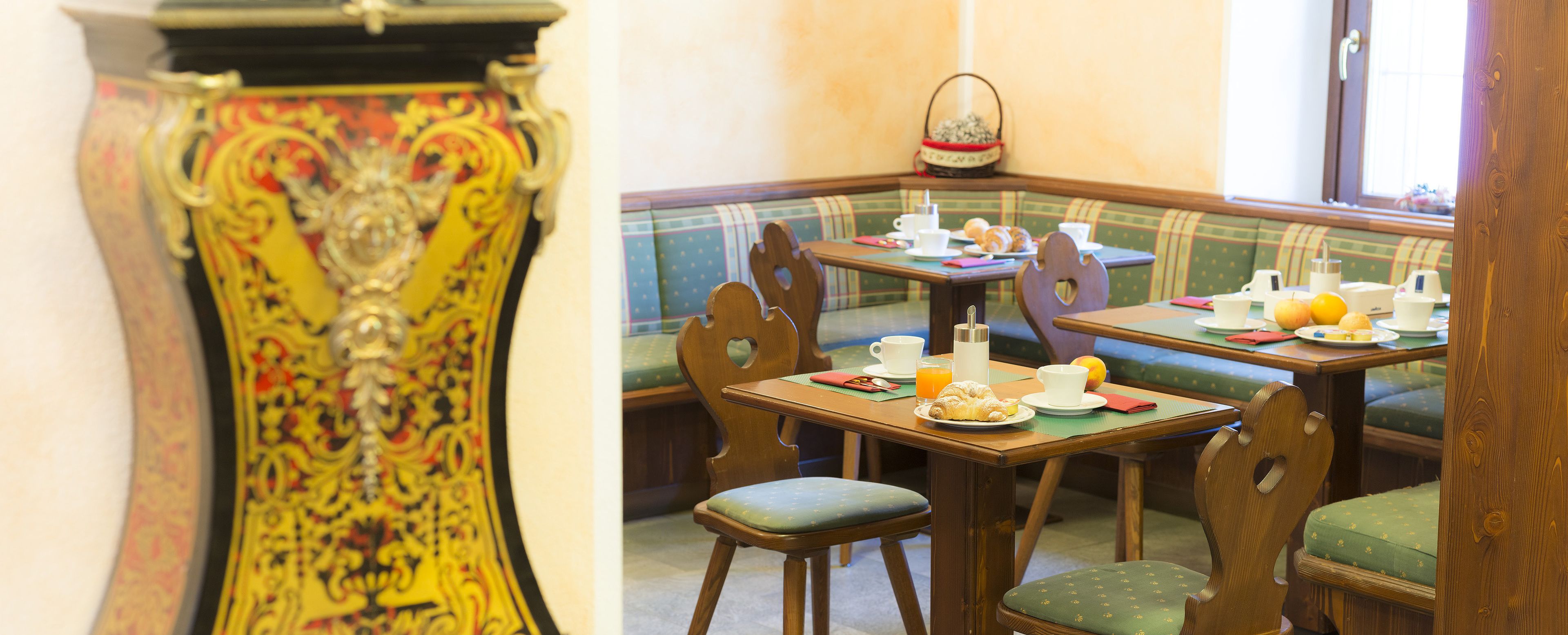 A corner of a room with a green upholstered bench, wooden chairs, and a table set with breakfast items.