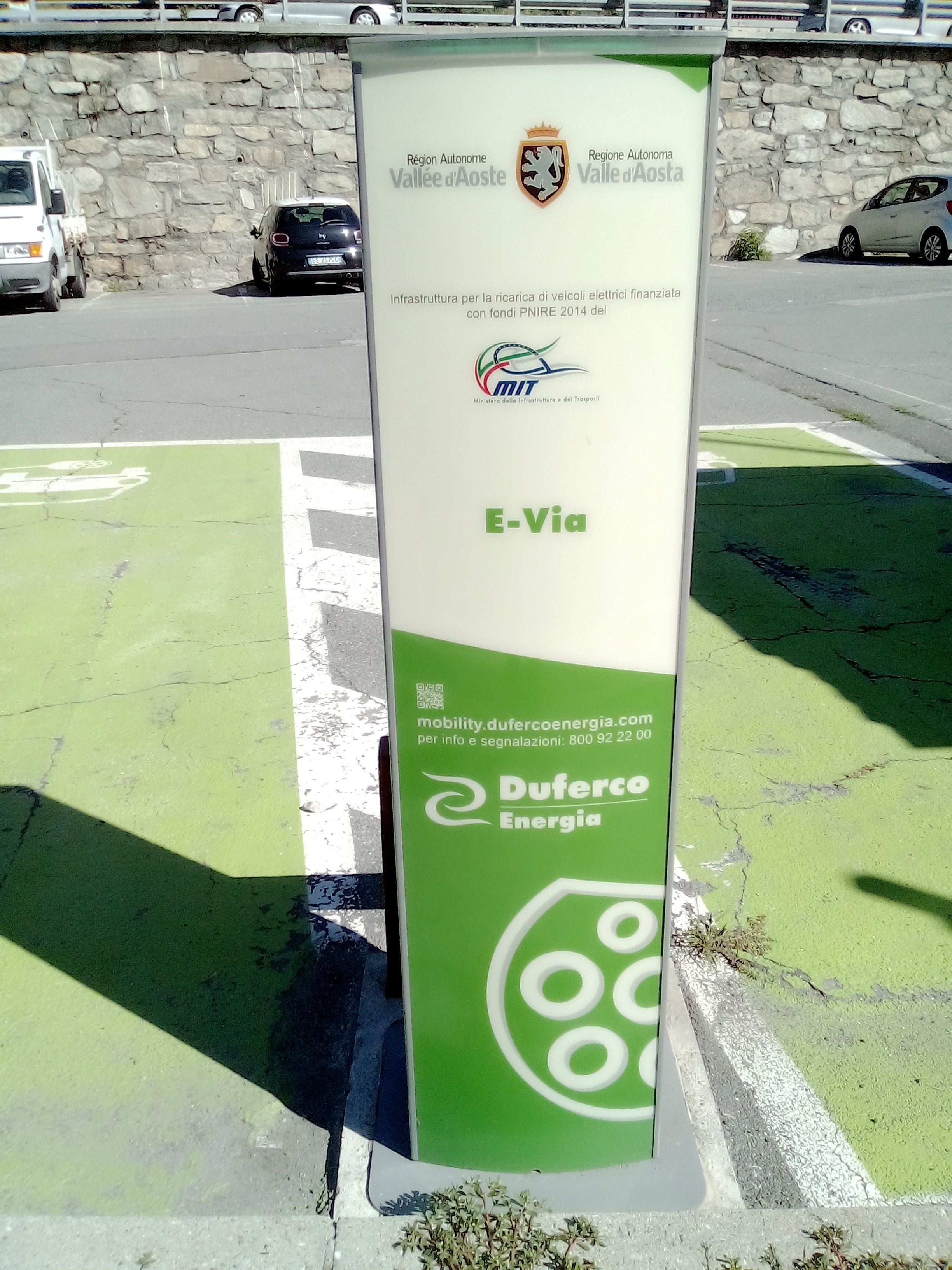Un cartel para una estación de carga de vehículos eléctricos, con los logotipos de Regione Autonoma Valle d'Aosta y MIT.