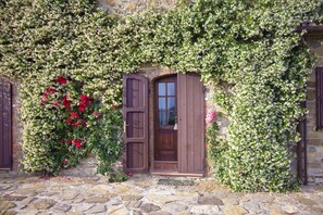 Un bâtiment en pierre avec une porte en bois et une fenêtre, le tout recouvert de plantes grimpantes et de fleurs.