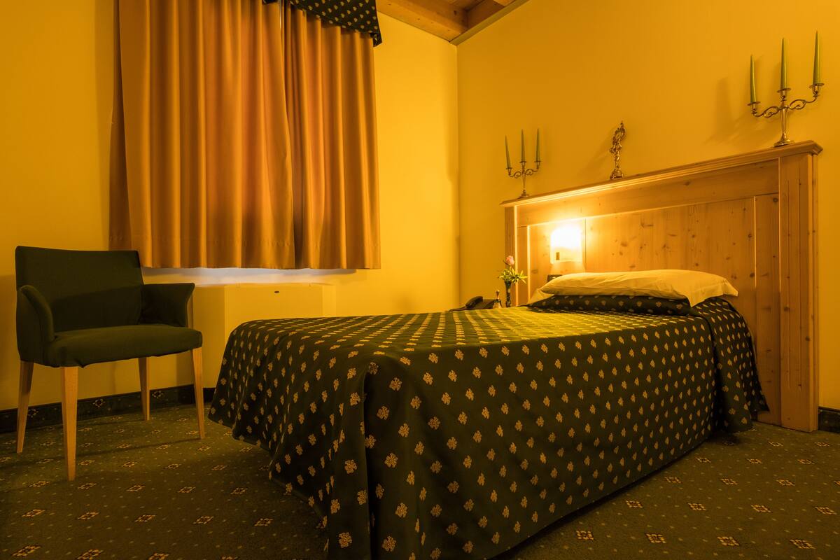 Une pièce comprenant un lit, une chaise, une fenêtre avec des rideaux et un chandelier fixé au mur.