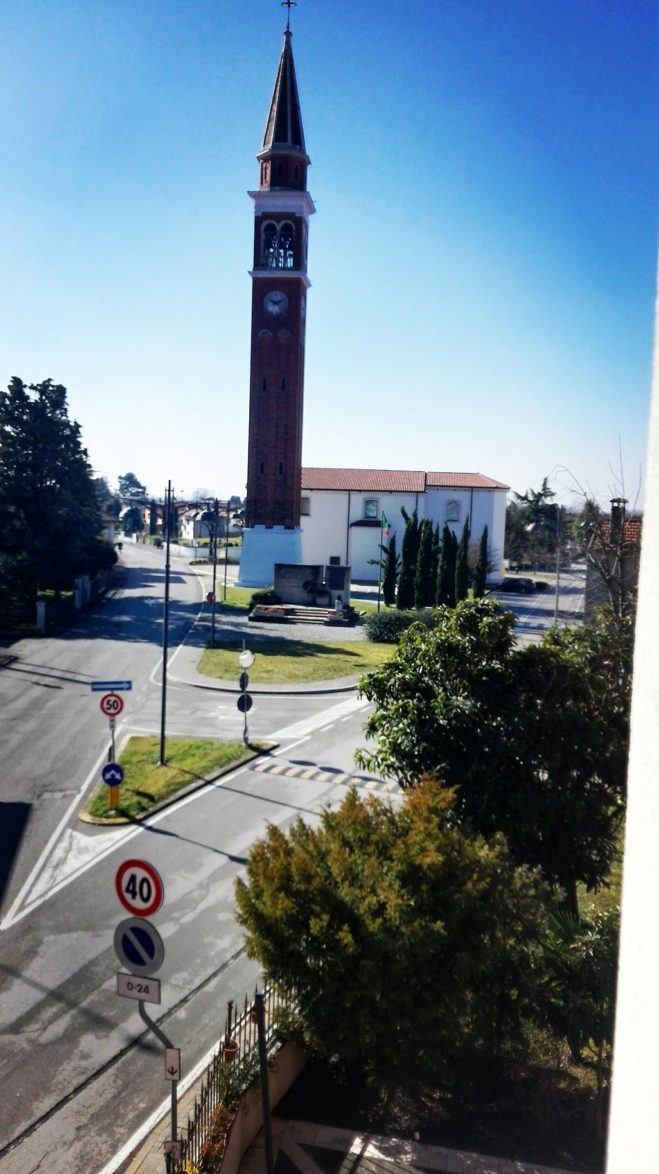 A church with a tall clock tower, a road with a speed limit sign, and a clear blue sky.