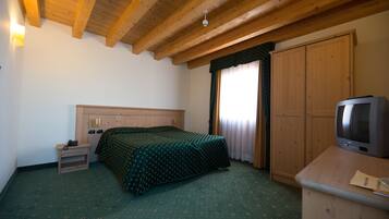 A bedroom with a wooden ceiling, a bed with a green bedspread, a wooden wardrobe, and a television on a wooden dresser.