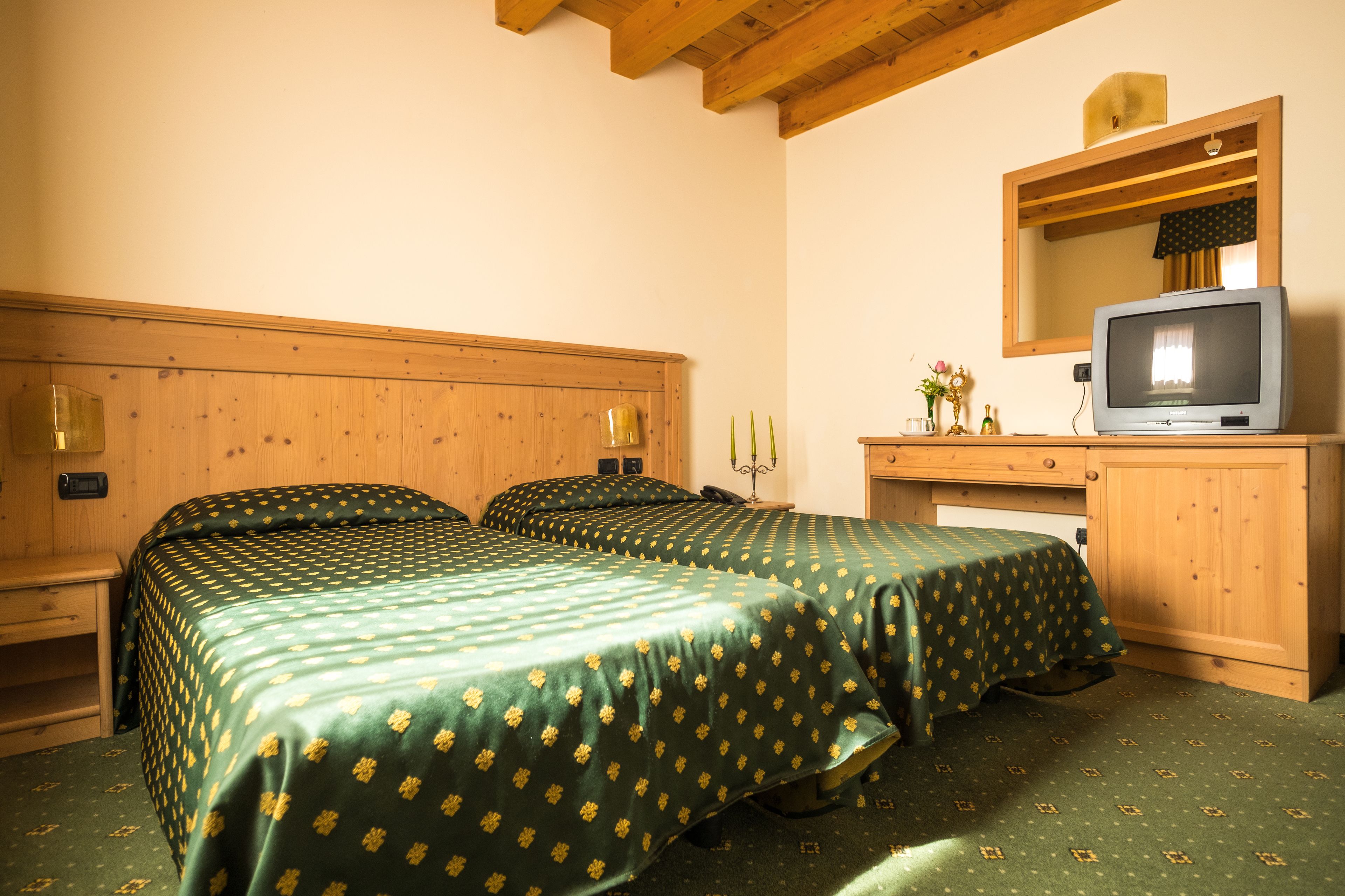 A room with two beds, wooden headboards, a wooden desk with a television, and a mirror above the desk.