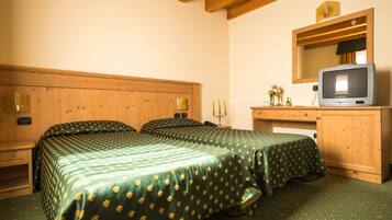 A room with two beds, wooden headboards, a wooden desk with a television, and a mirror above the desk.