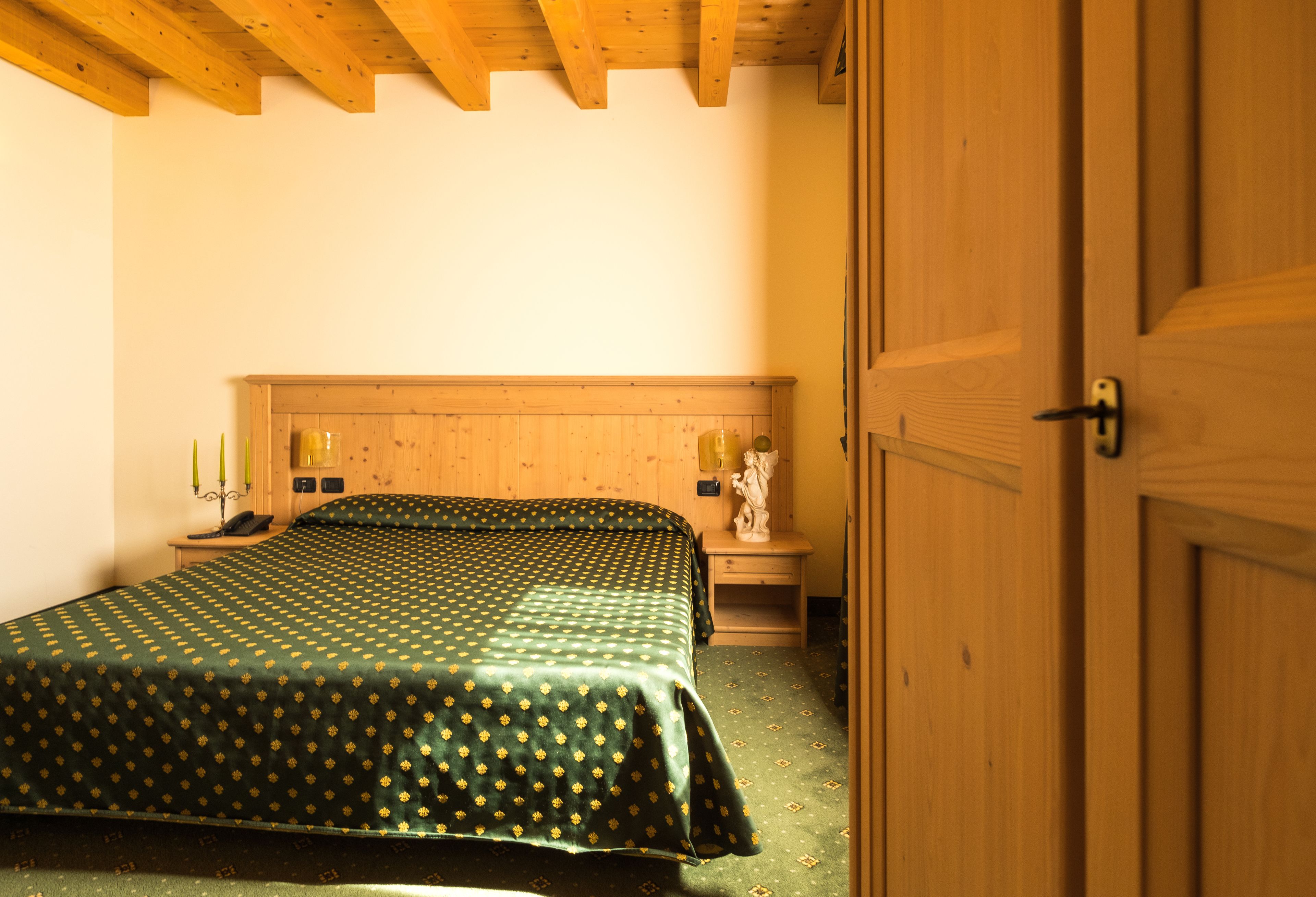 Une chambre à coucher avec une tête de lit en bois, une couvre-lit à motifs verts, une table de chevet avec une lampe et une petite table de nuit avec un téléphone.