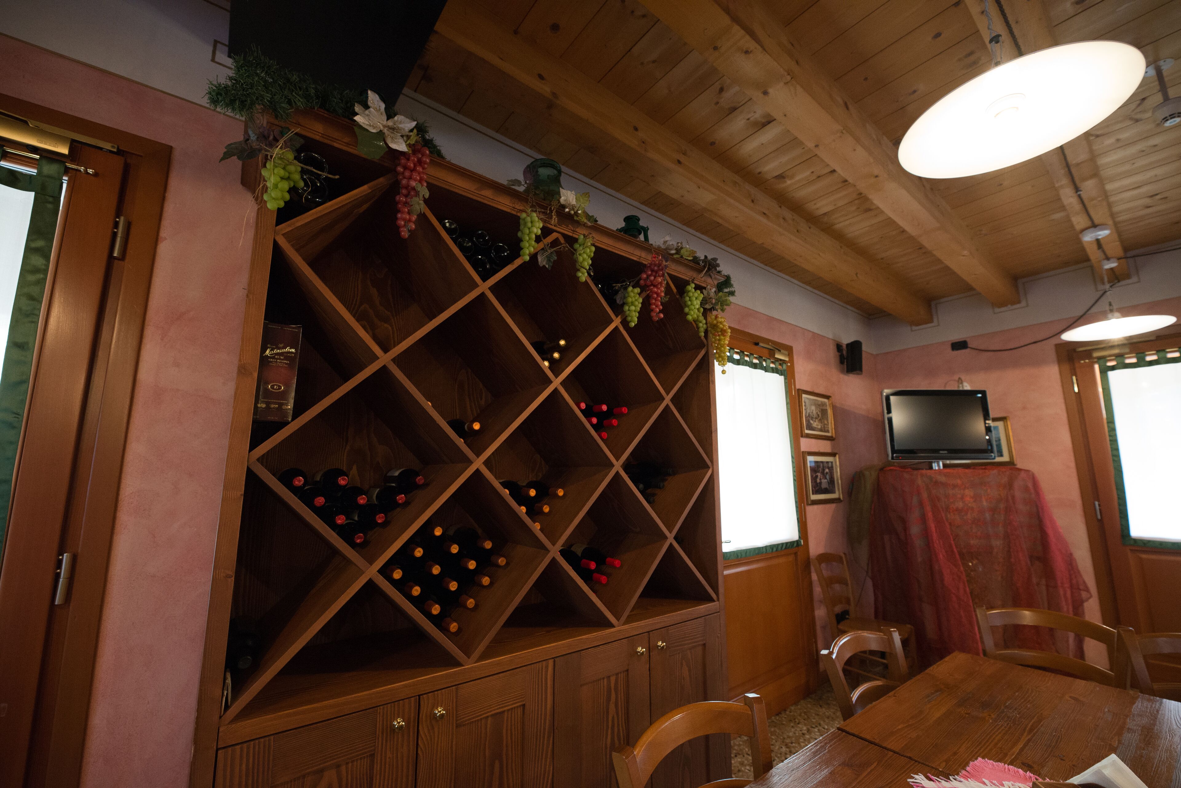 A room with a wooden wine rack, a dining table, chairs, and a television on a table.