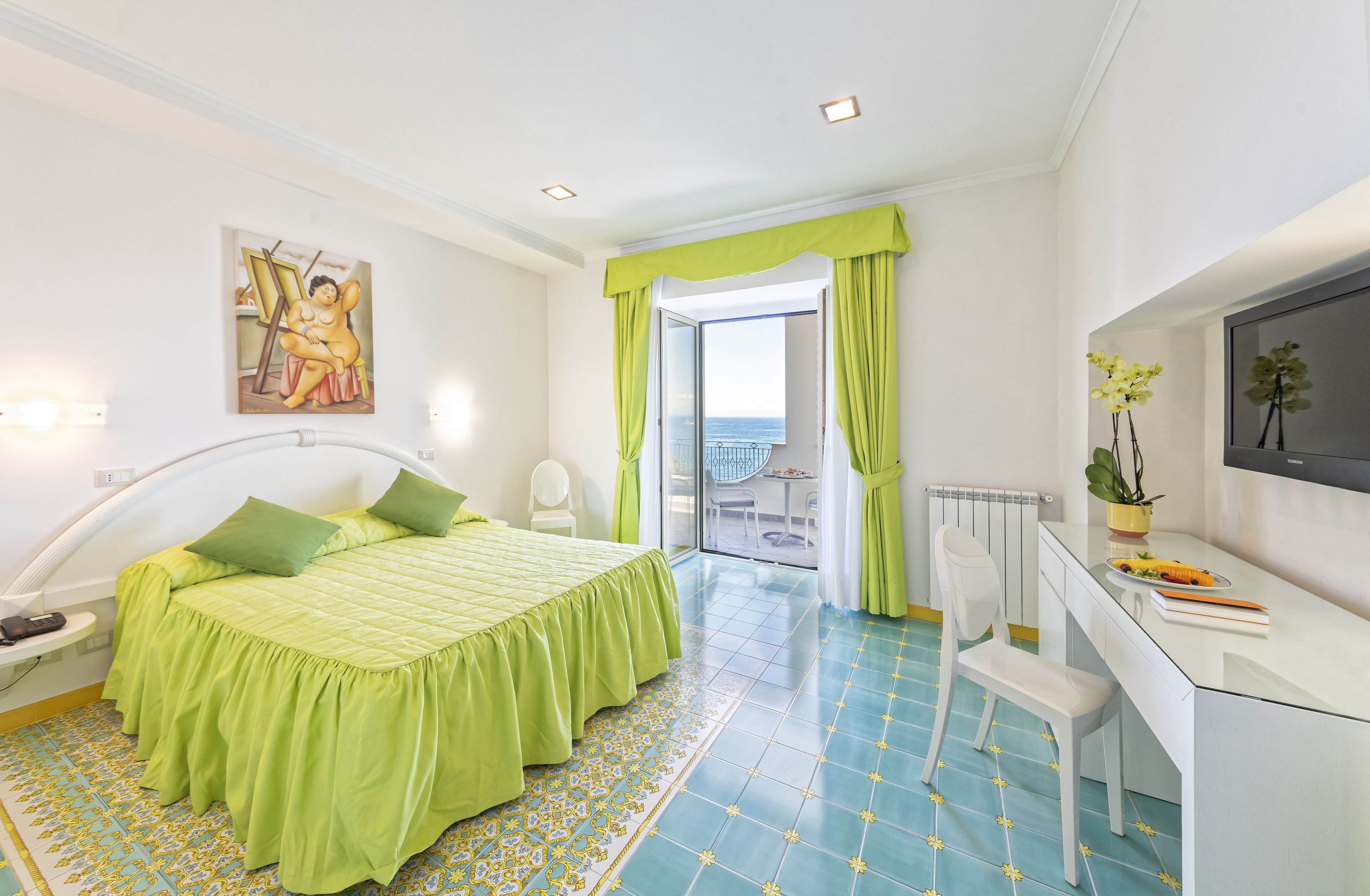Une chambre d’hôtel équipée d’un lit, d’un bureau, d’une chaise, d’une télévision et d’un balcon avec vue.