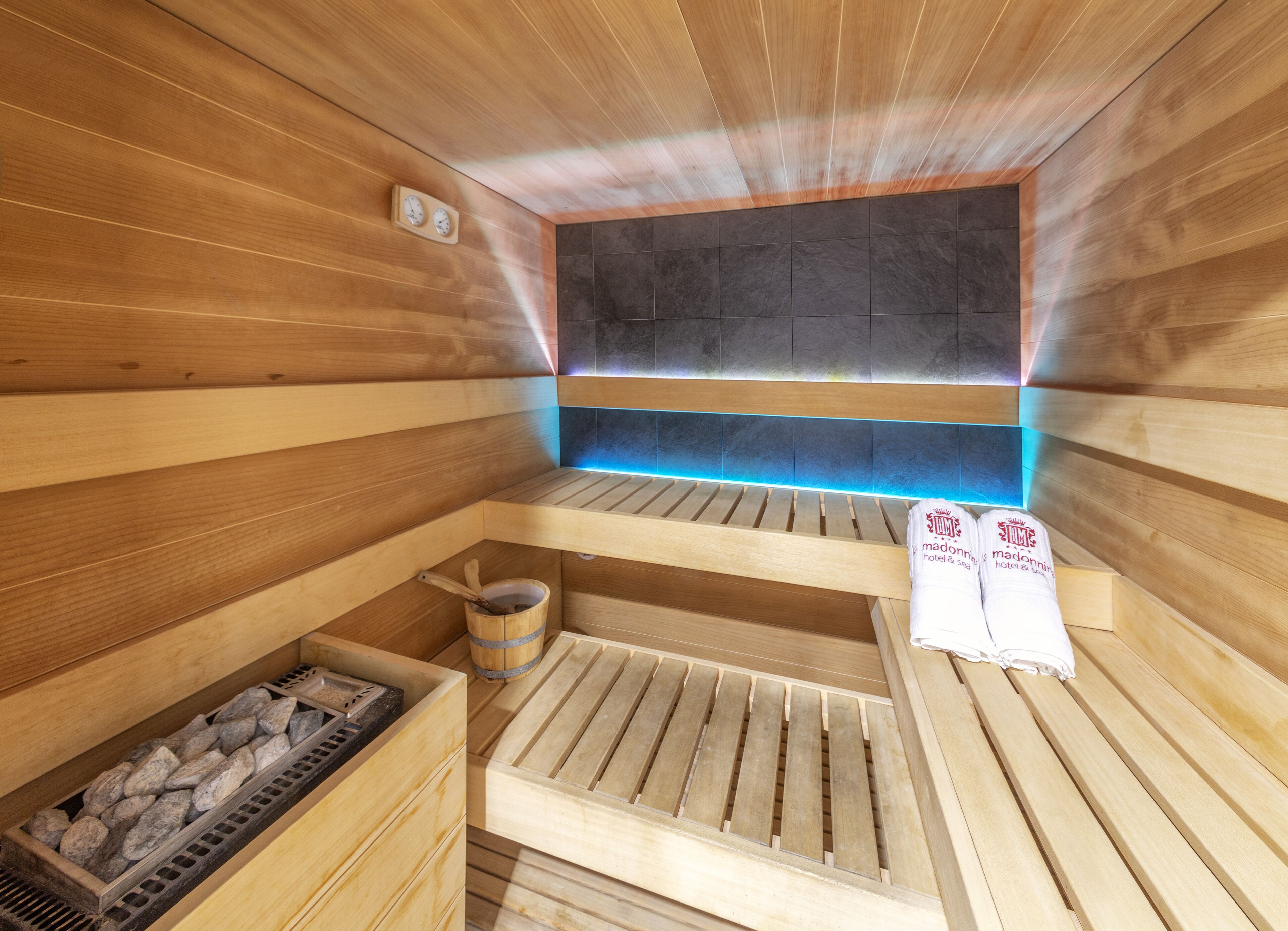 A wooden sauna with benches, a stone wall, and a blue-lit shelf.