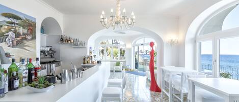 A modern kitchen with a bar area, white furniture, and a view of the sea.