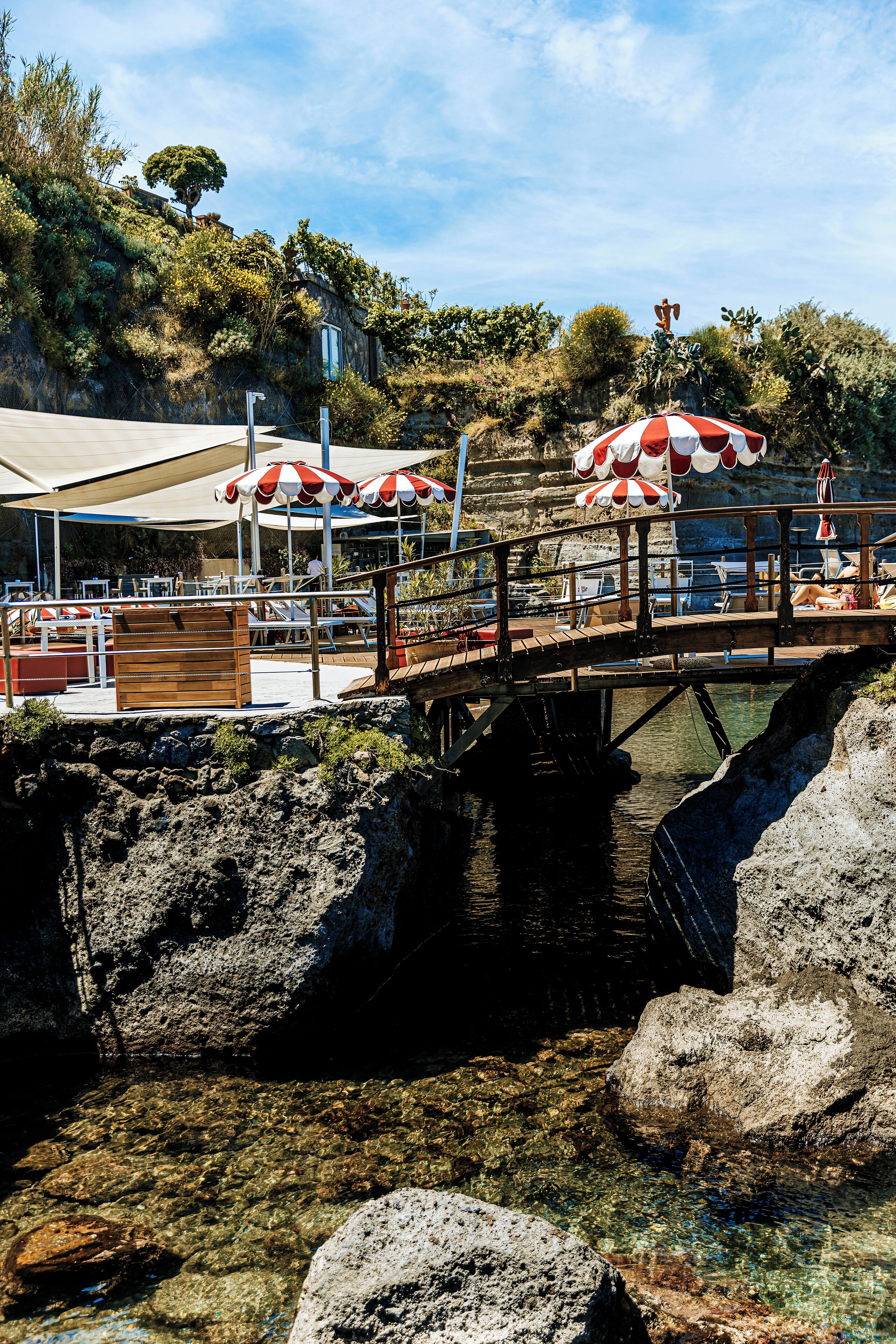 A pier with a wooden walkway, clear water, and red and white umbrellas.