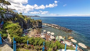 Un hôtel situé sur la côte, avec une plage rocheuse, une eau d’un bleu cristallin et une vue sur des îles lointaines.