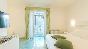 A hotel room with a bed, a TV, a desk, and a view of the outside balcony.