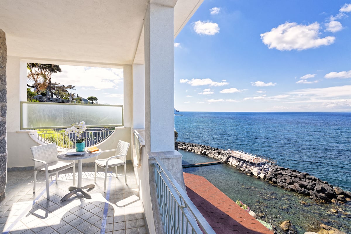 Ein Balkon mit Meerblick, einem Blumentopf und einem Tisch mit Stühlen.