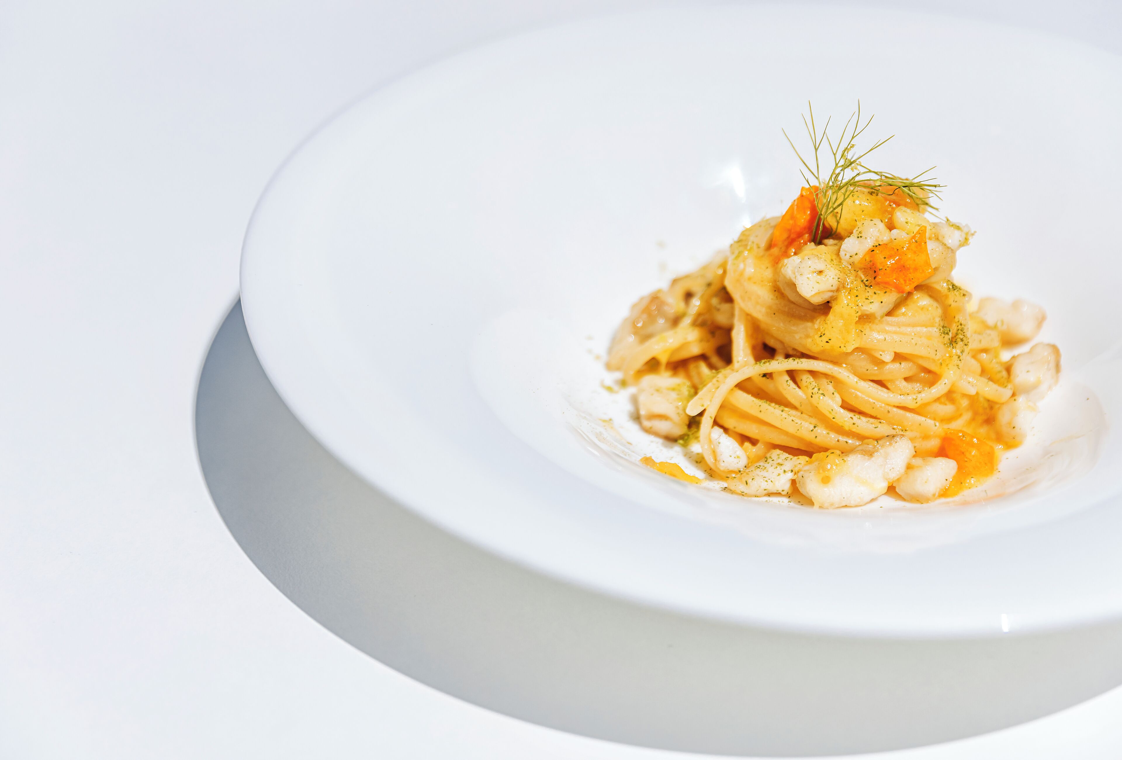 Une assiette blanche contenant un plat de pâtes, garni d’herbes et d’une décoration.