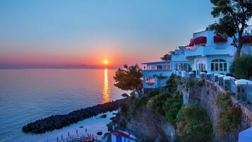 A coastal hotel with a view of the sunset over the sea, a pool area, and a cliffside location.