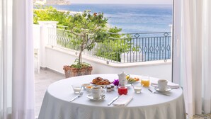 Une table sur le balcon, avec des aliments pour le petit-déjeuner, et une vue sur la mer.