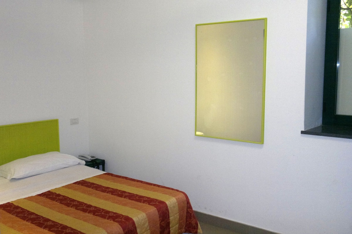 A simple room with a bed, a nightstand, and a wall-mounted mirror.
