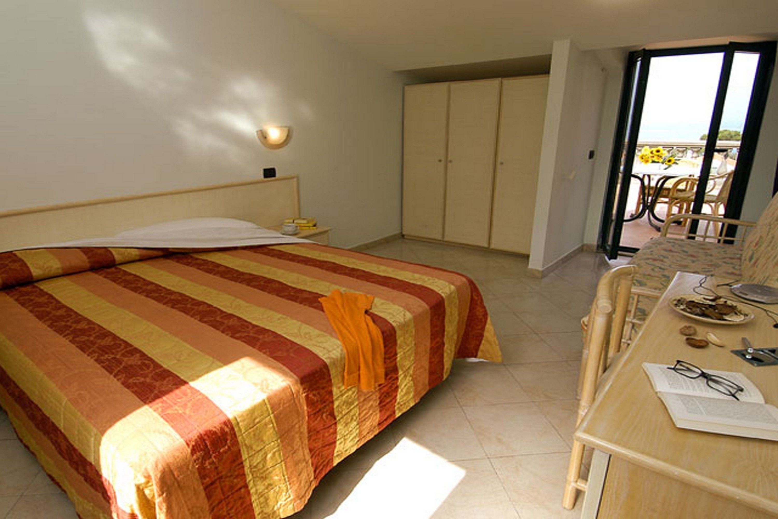 A hotel room with a bed, a desk, and a balcony with chairs.