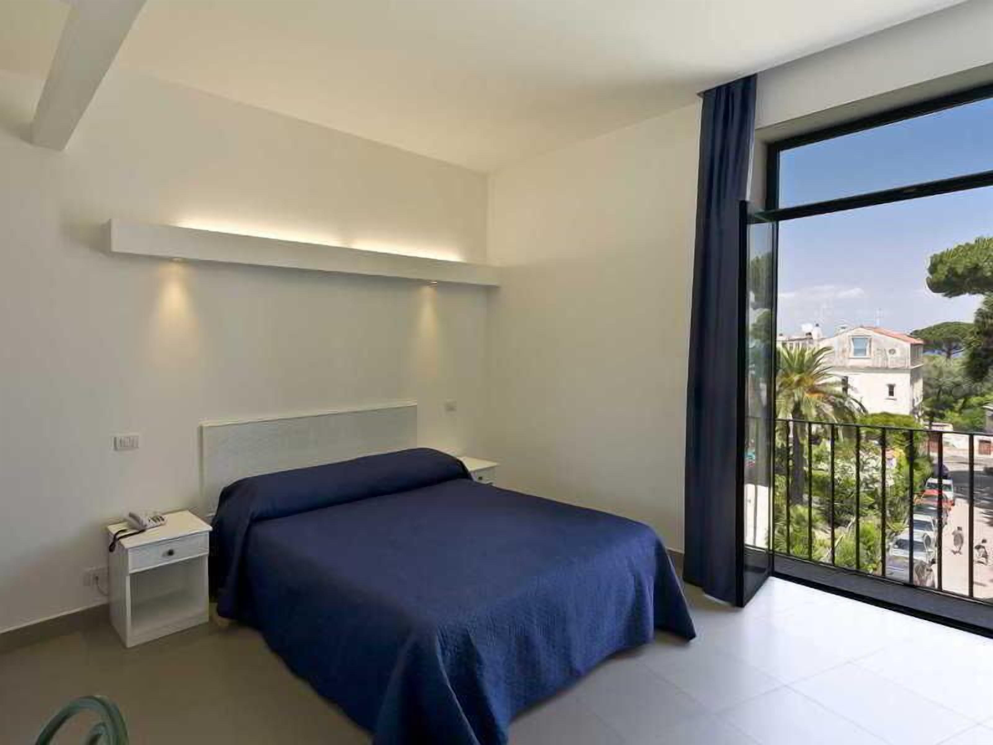 A modern bedroom with a bed, bedside table, and a large window with a view of the outside.