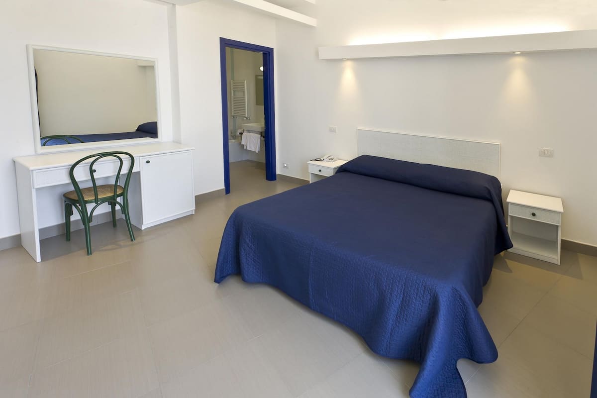 A bedroom with a bed, a desk, a chair, and a mirror.