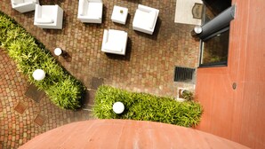 Un patio en la azotea con mobiliario exterior blanco, suelo de ladrillo y setos verdes.