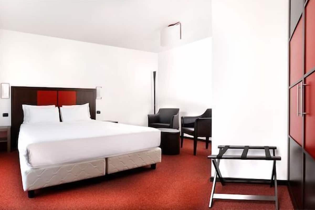 A hotel room with a large bed, a desk, a chair, and a wardrobe.