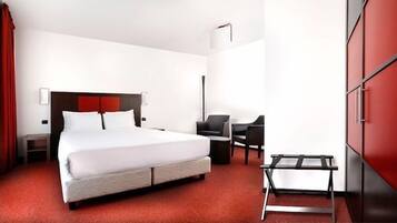 A hotel room with a large bed, a desk, a chair, and a wardrobe.