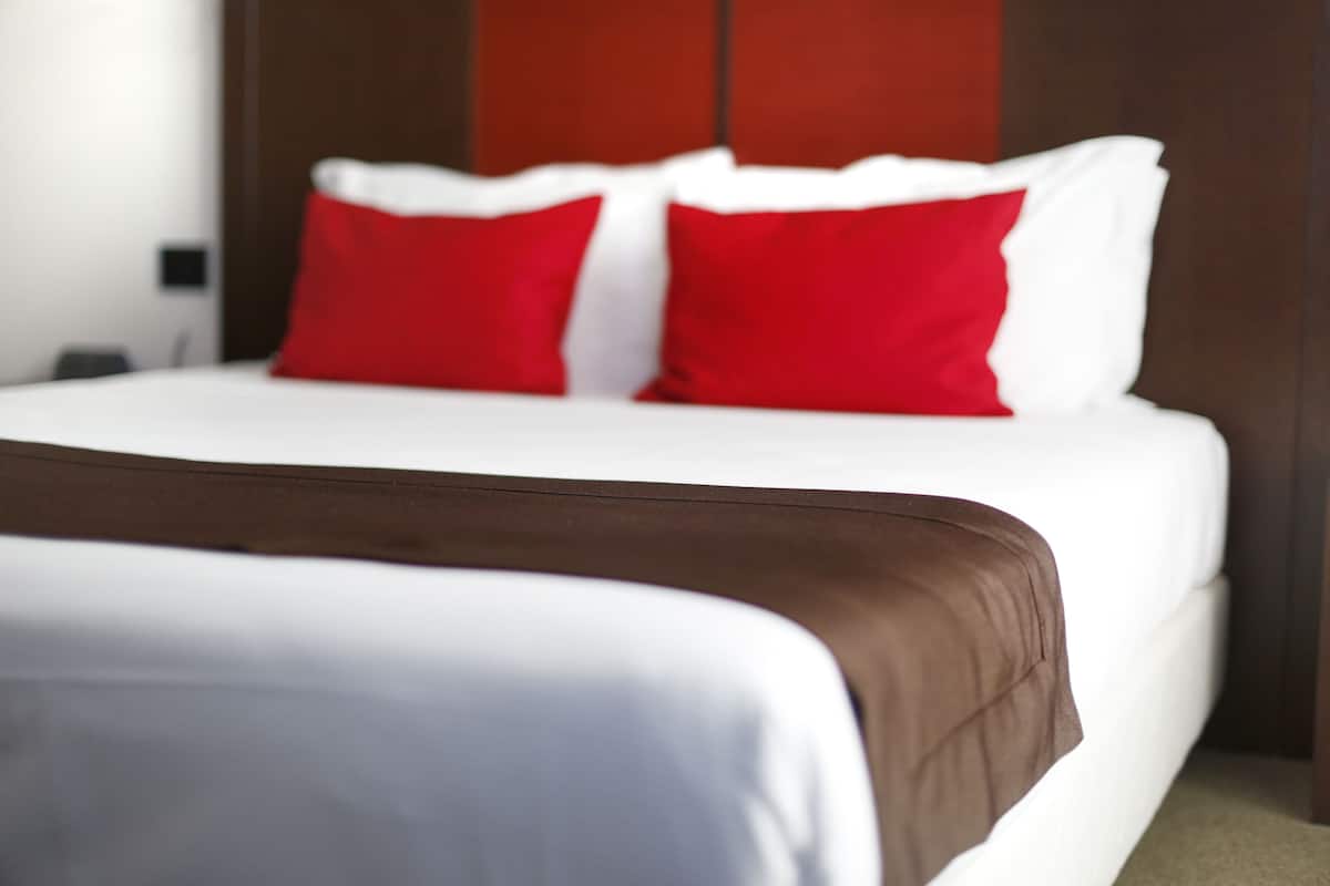 A bed with white and red bedding, a brown headboard, and a wooden panel wall.