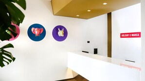 Una zona de recepción con un mostrador blanco, tres adornos circulares en la pared y un cartel que dice "HOLIDAY LA MARCA SMART HOTEL".