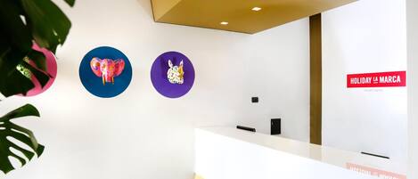 Una zona de recepción con un mostrador blanco, tres adornos circulares en la pared y un cartel que dice "HOLIDAY LA MARCA SMART HOTEL".