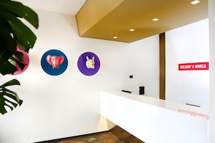 Una zona de recepción con un mostrador blanco, tres adornos circulares en la pared y un cartel que dice "HOLIDAY LA MARCA SMART HOTEL".