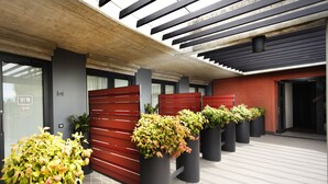 Una entrada moderna a un edificio con un portón rojo, plantas en macetas y suelo de baldosas.
